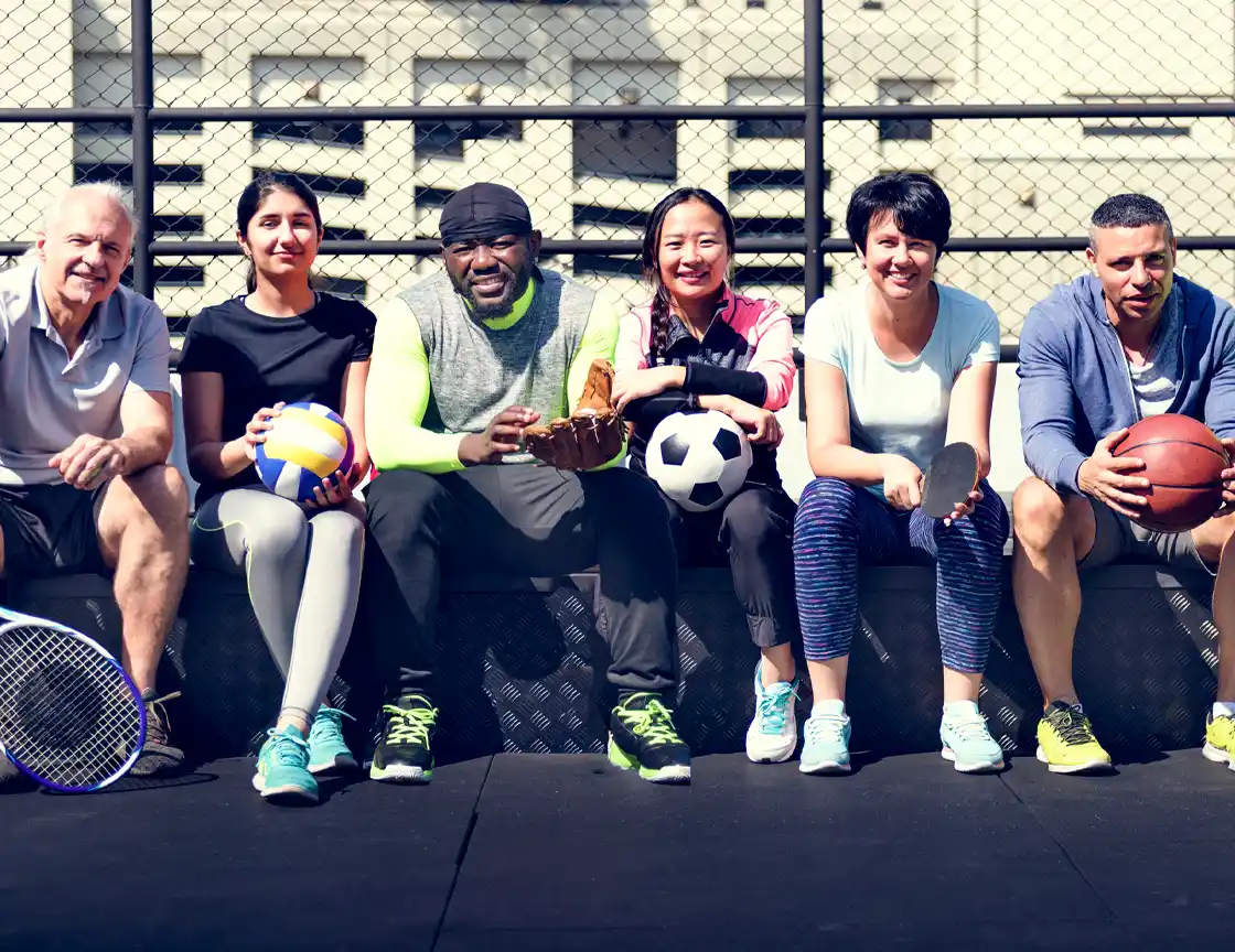 A group of friends of diverse genders, ages, and races playing sports in a multi-purpose court.